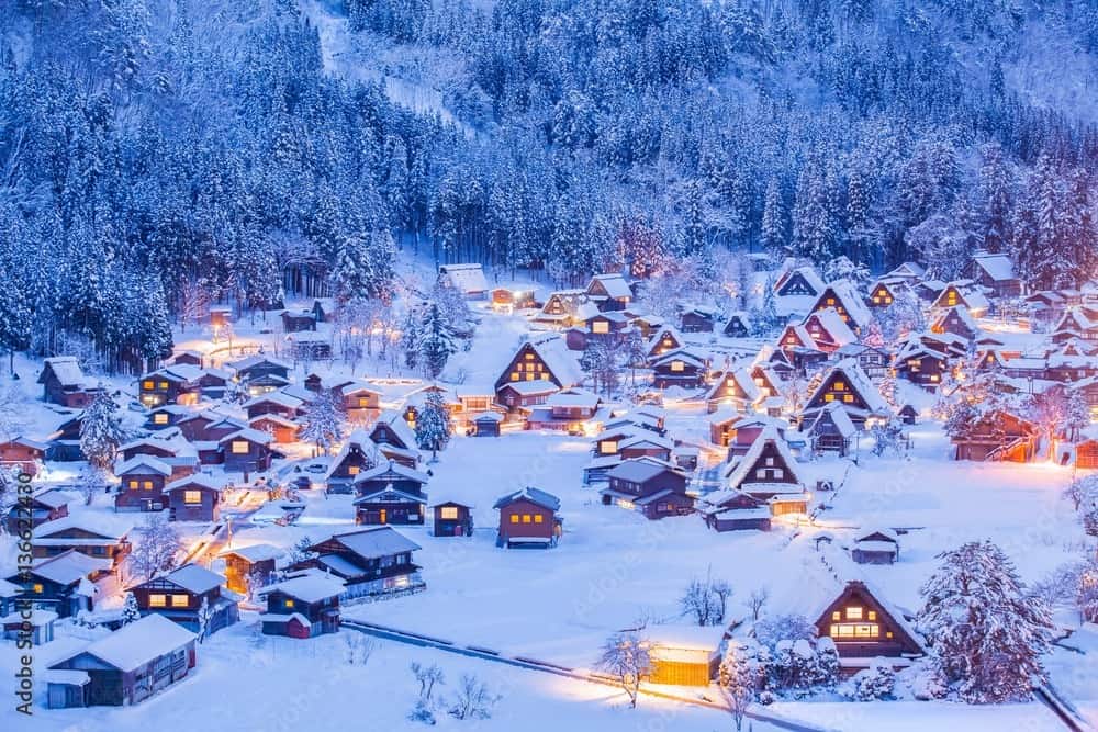 Snow-covered thatched houses lit up at night in a Japanese mountain village