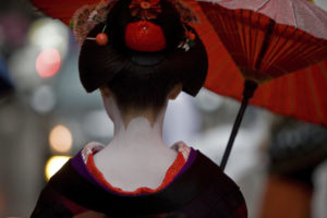 The back of a Geisha holding a red parasol