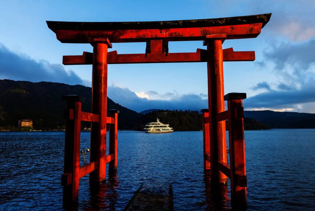 Japan group travel to Hakone: a red torii gate stands in Lake Ashi with a sightseeing boat beyond