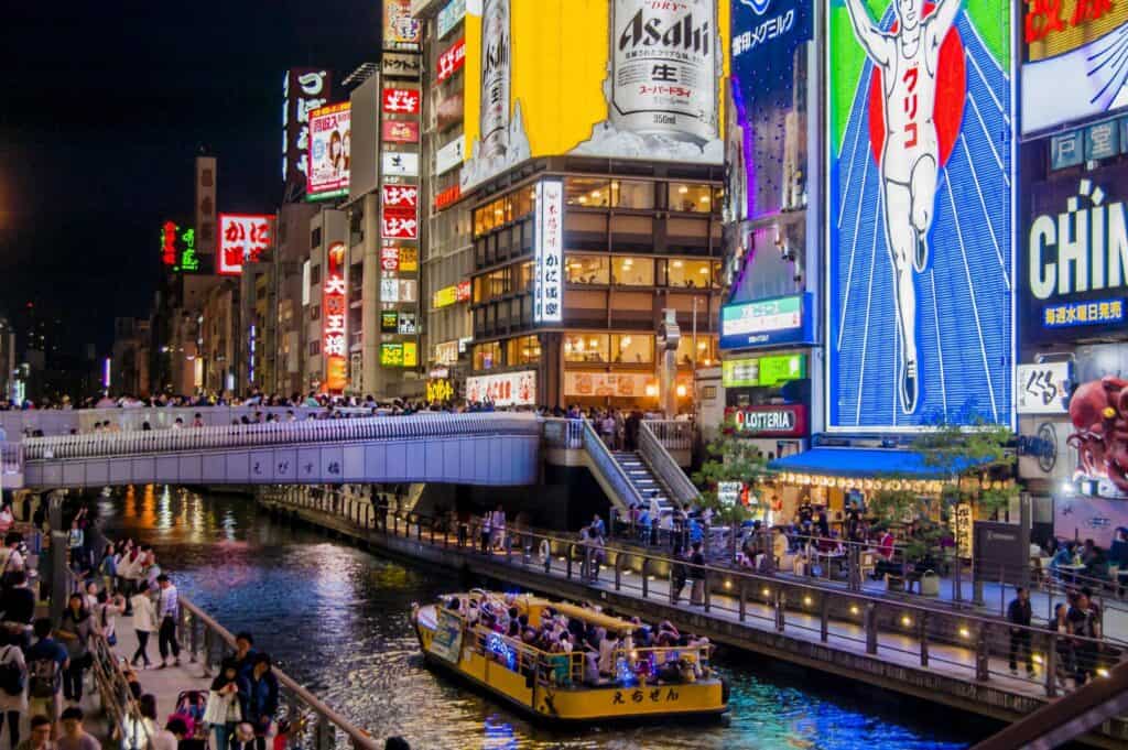 The Dotonbori canal in Osaka at night with neon signs and a tour boat on the water
