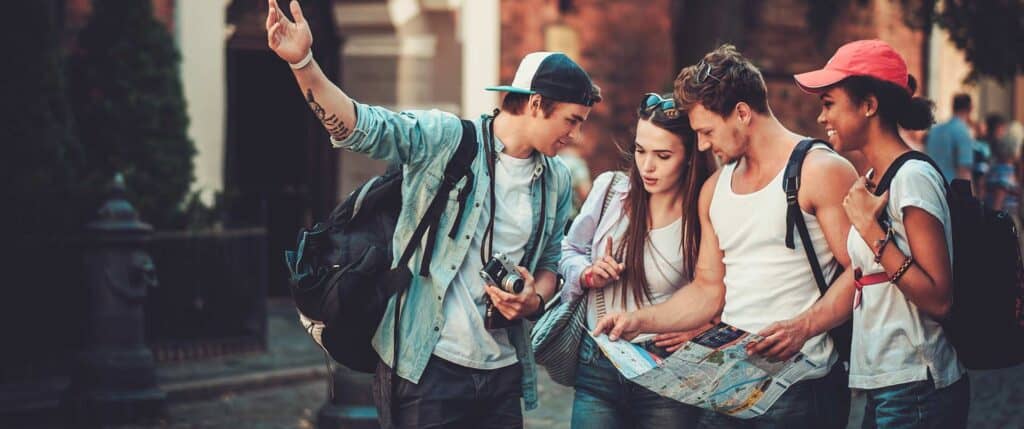 Four young friends with backpacks studying a city map together while sightseeing in Japan