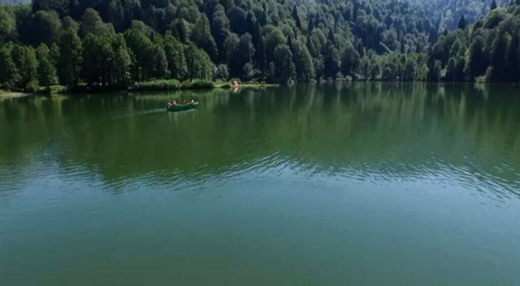 A still green lake framed by forest, with a single small boat on the water