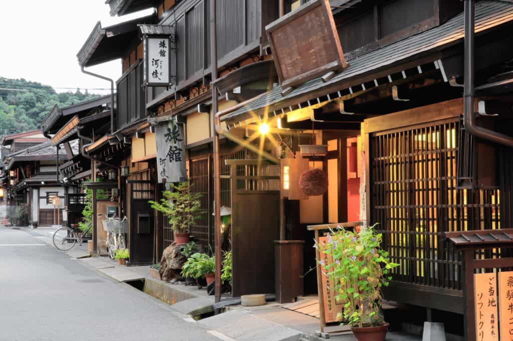 A lantern-lit street of dark wooden inns and shops in an old mountain town at dusk