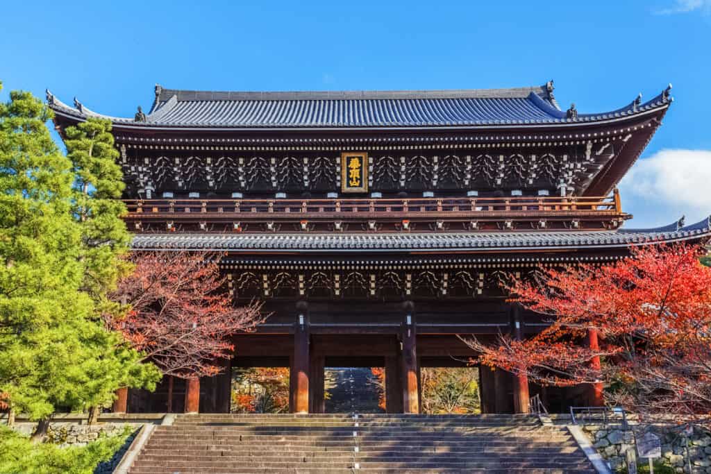 The massive two-story wooden gate of Chion-in under a blue sky with autumn maples