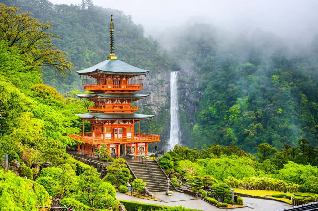 A vermilion three-story pagoda before Nachi Falls in the forested mountains of the Kumano Kodo in rural Japan