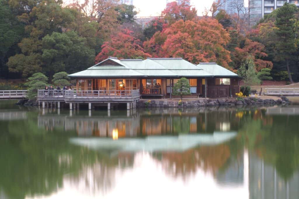 A teahouse on a lake framed by autumn leaves
