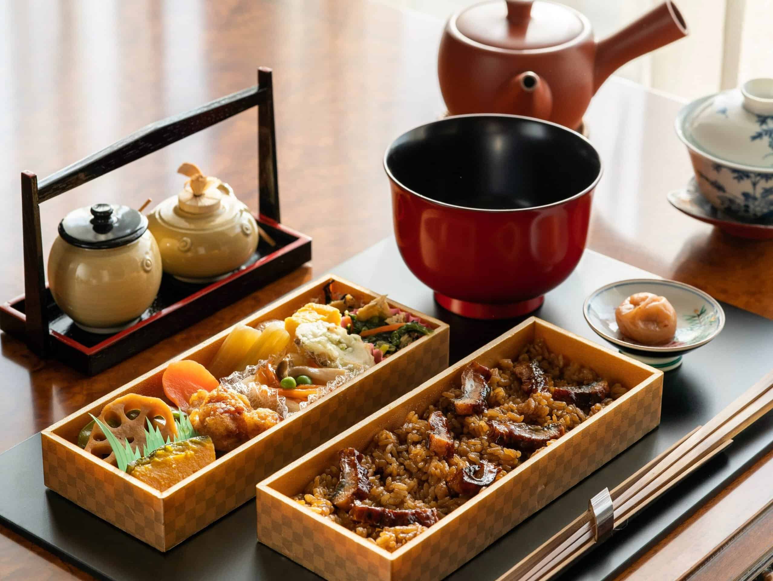 A traditional Japanese bento box of rice, grilled eel and vegetables beside tea