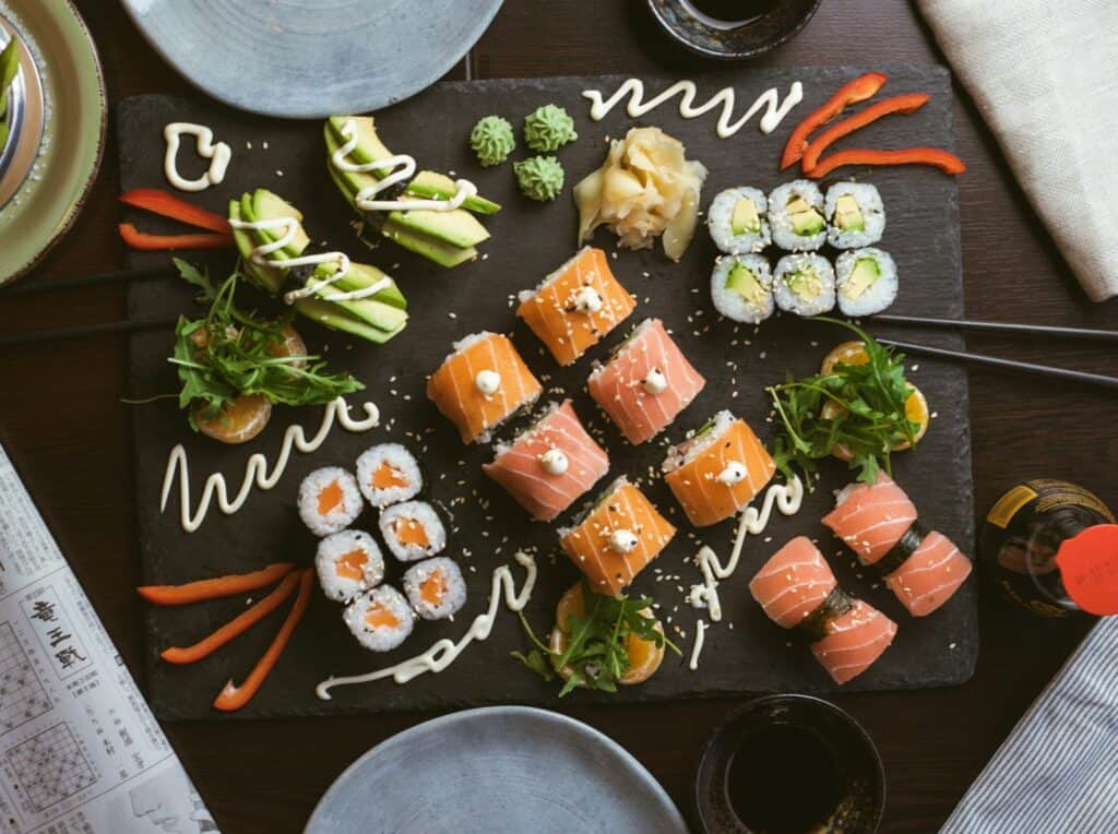A dark slate platter of colorful sushi rolls and sashimi with garnishes, set for sharing