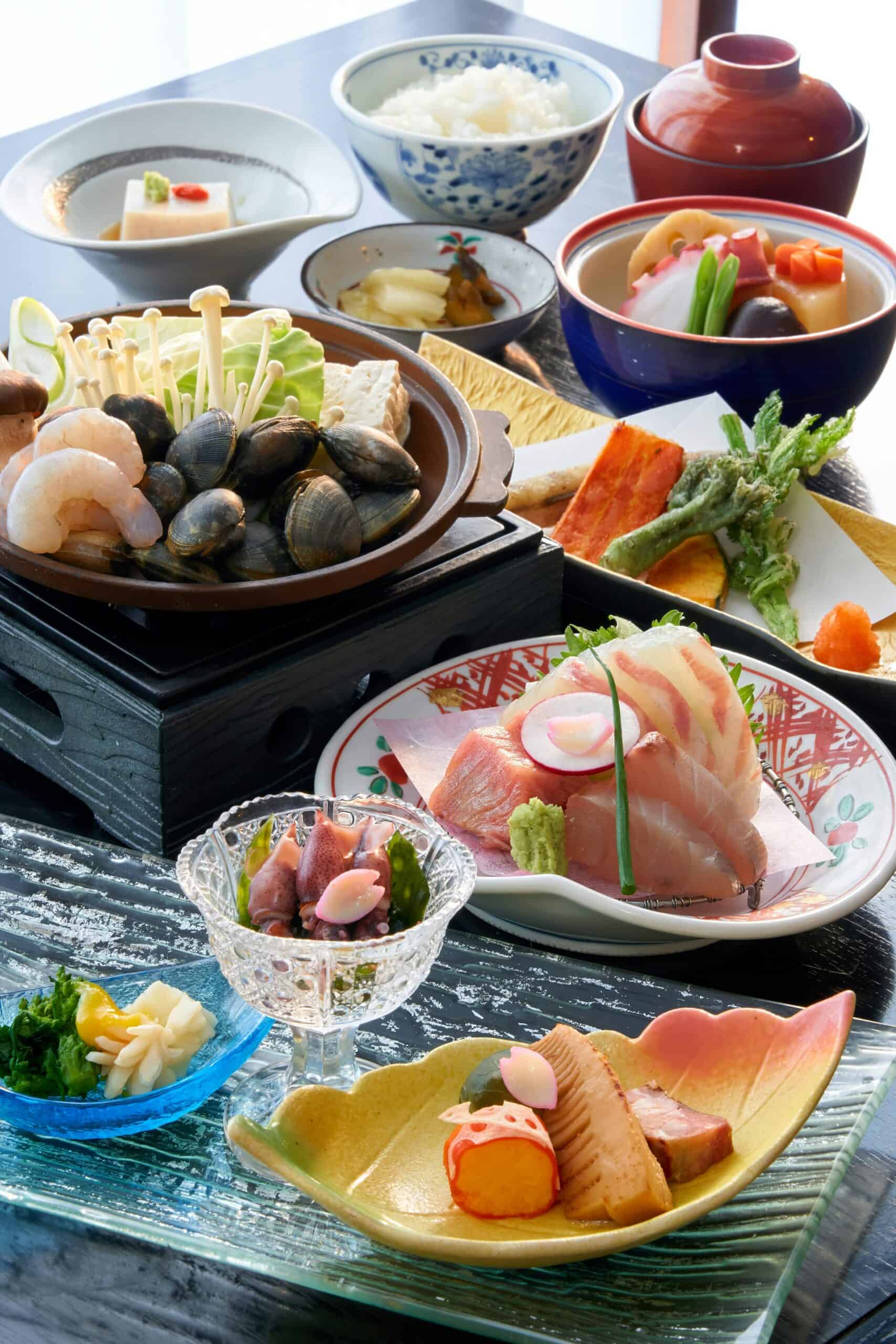 A tall arrangement of Japanese dishes with sashimi, simmered vegetables and small plates on a glass tray