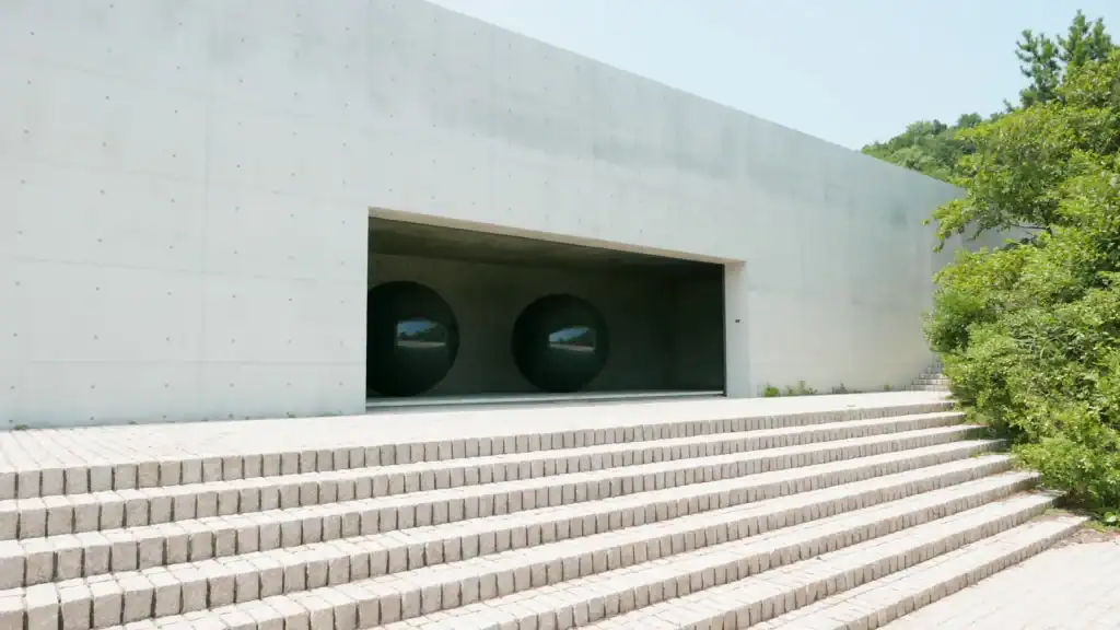 A plain concrete gallery wall with a long dark opening and wide stone steps on Naoshima