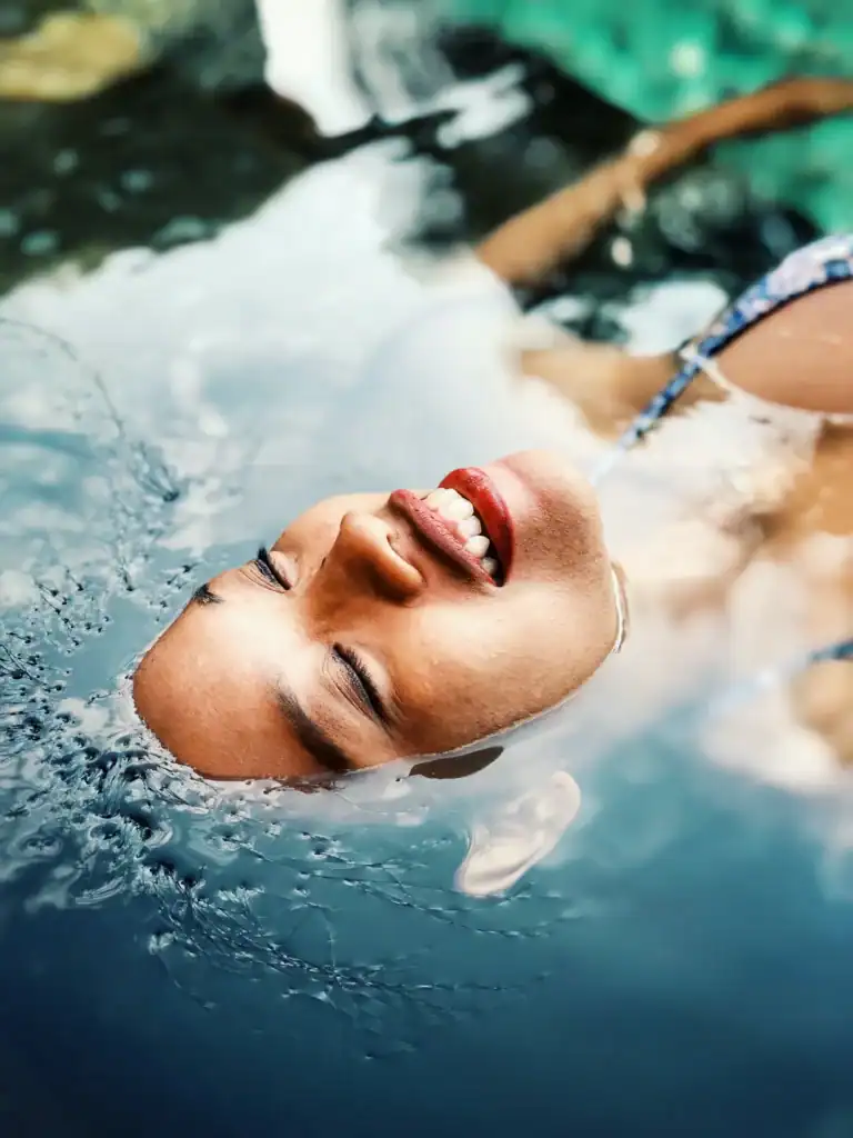 A smiling young woman floating on her back in clear blue water, eyes closed