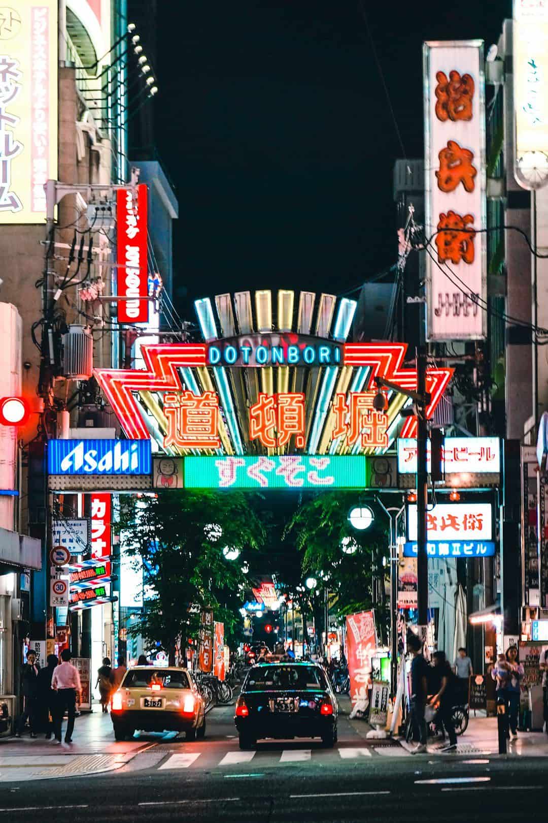 A Japanese city street at night with neon signs and busy traffic