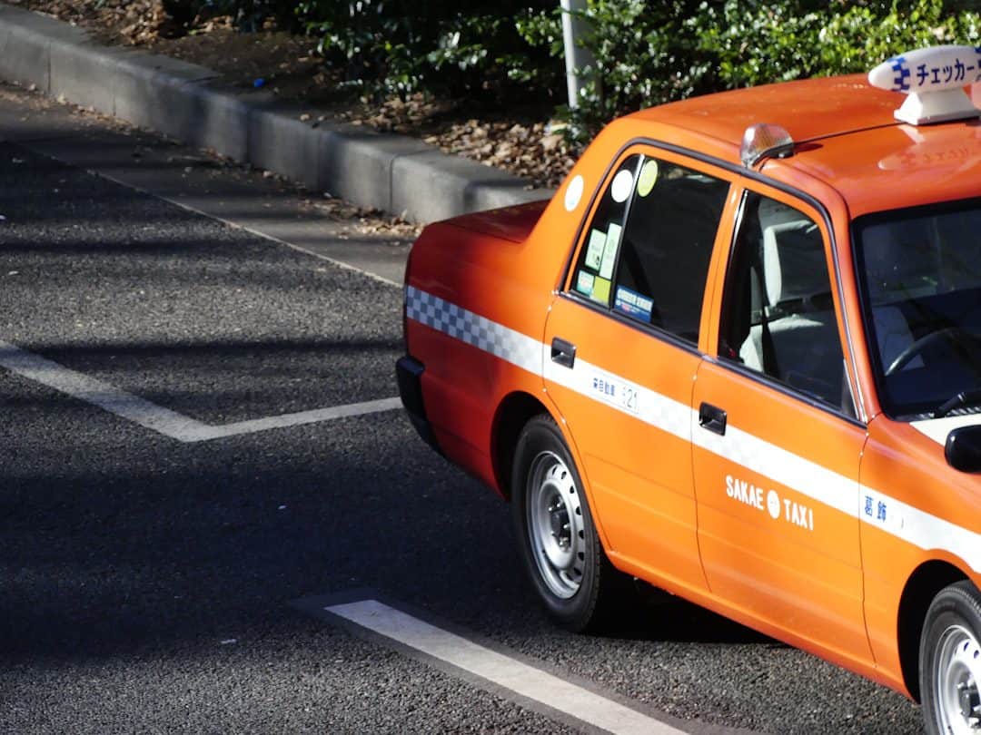 An orange Tokyo taxi with a checkered stripe driving along a city street