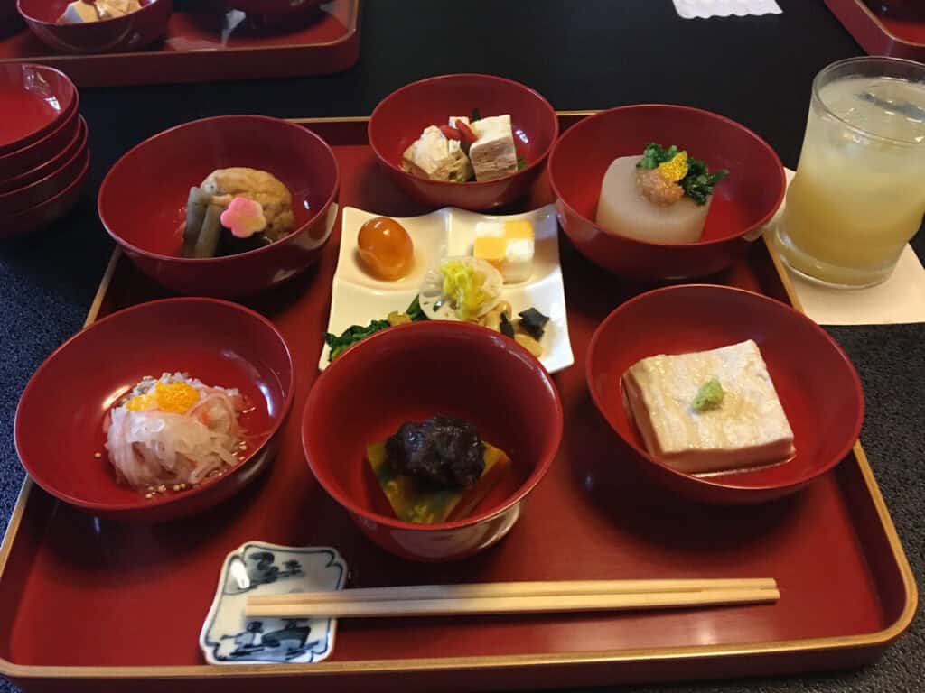 A red lacquer tray of shojin ryori with simmered vegetables, tofu and small dishes in lacquer bowls