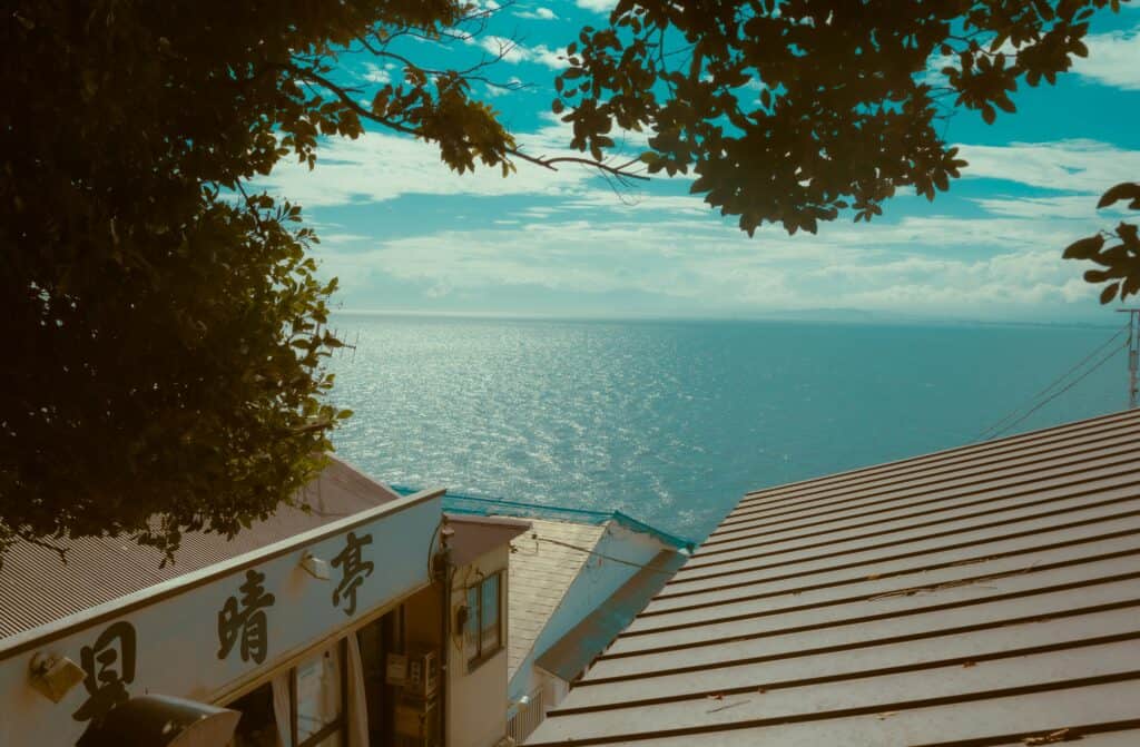 A view over a tiled roof to a calm blue sea framed by branches