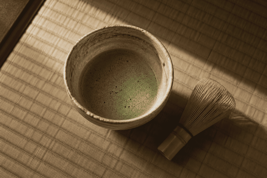 A bowl of frothy matcha with a bamboo whisk on a tatami mat