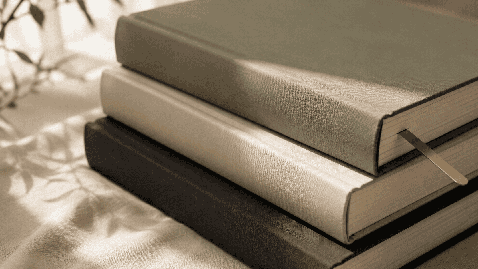 Three large-format Studio Ghibli art books stacked on cream linen with a brass bookmark