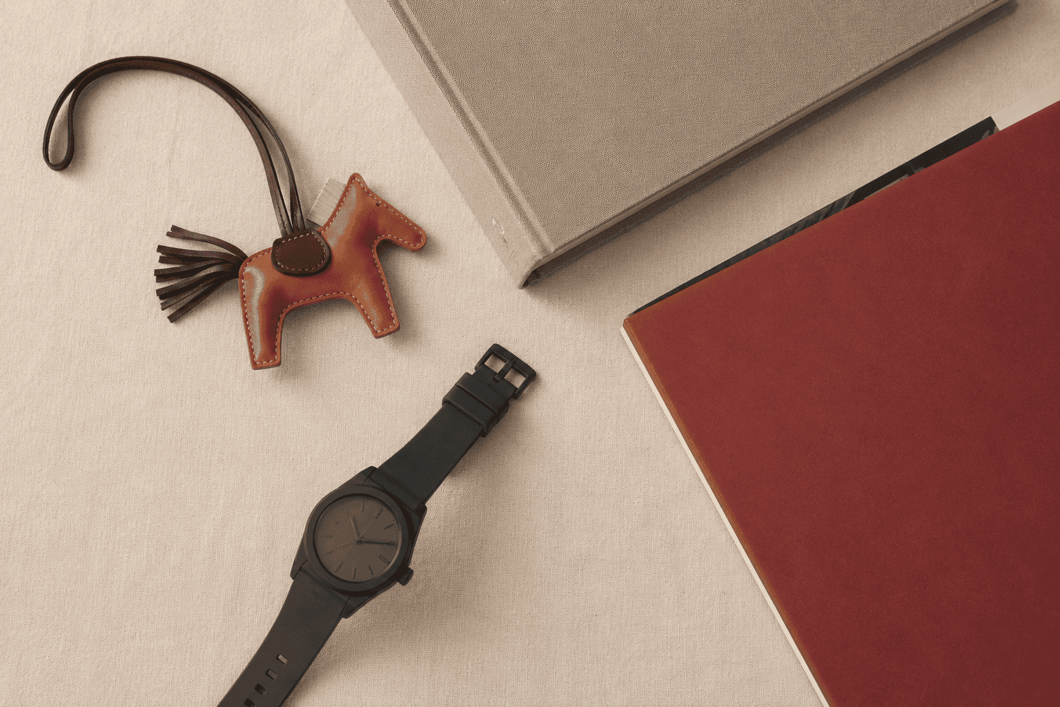A considered flatlay of luxury anime objects — a leather charm, an art book, a vinyl record, and a collaboration watch on cream linen