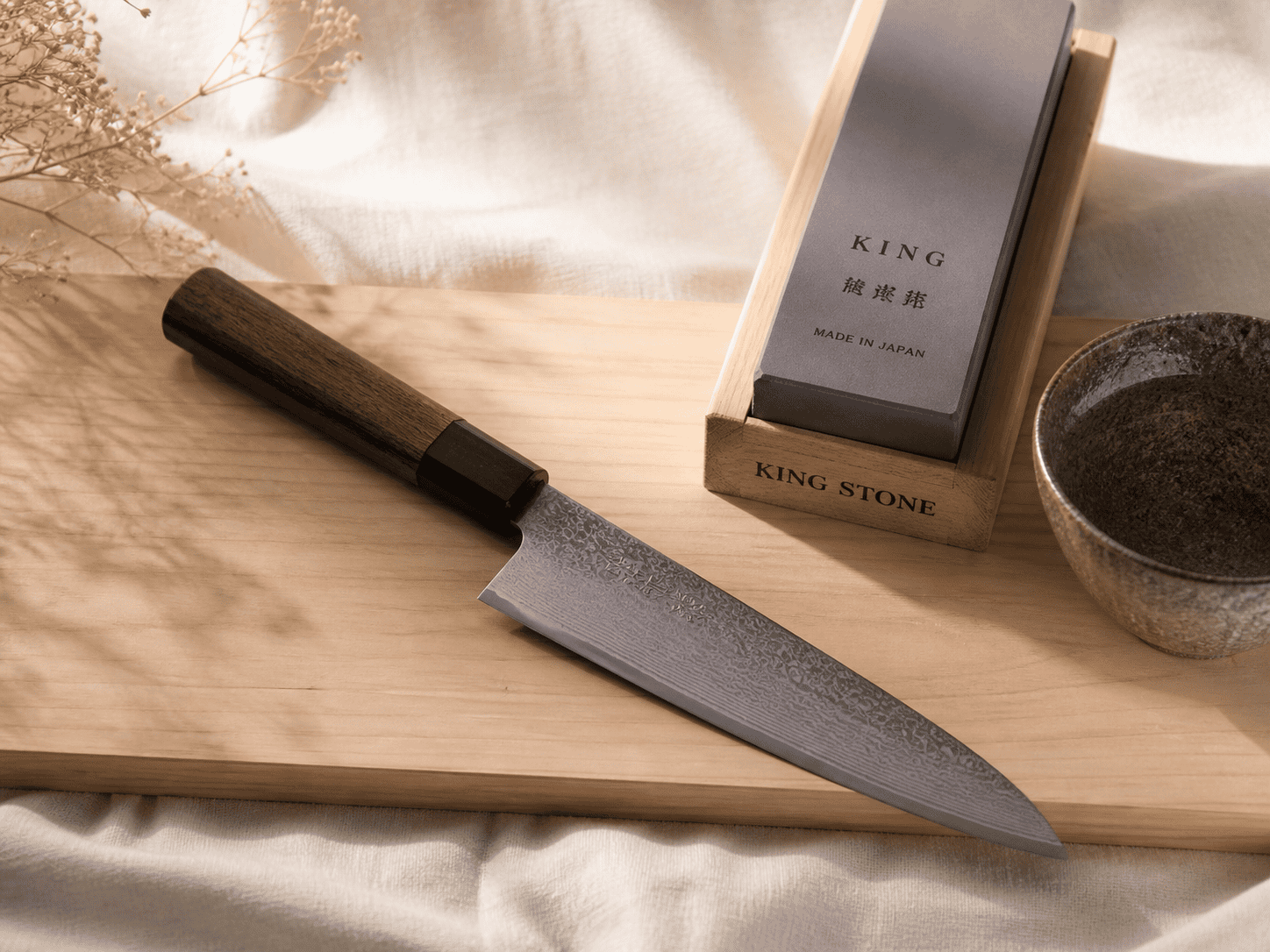 A Japanese chef's knife on a hinoki cypress cutting board, with a whetstone beside it