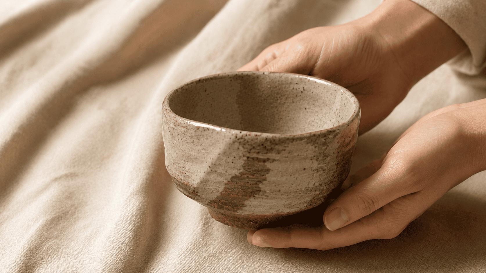 A handcrafted Japanese tea bowl held in a craftsman's hands — the home craft tradition