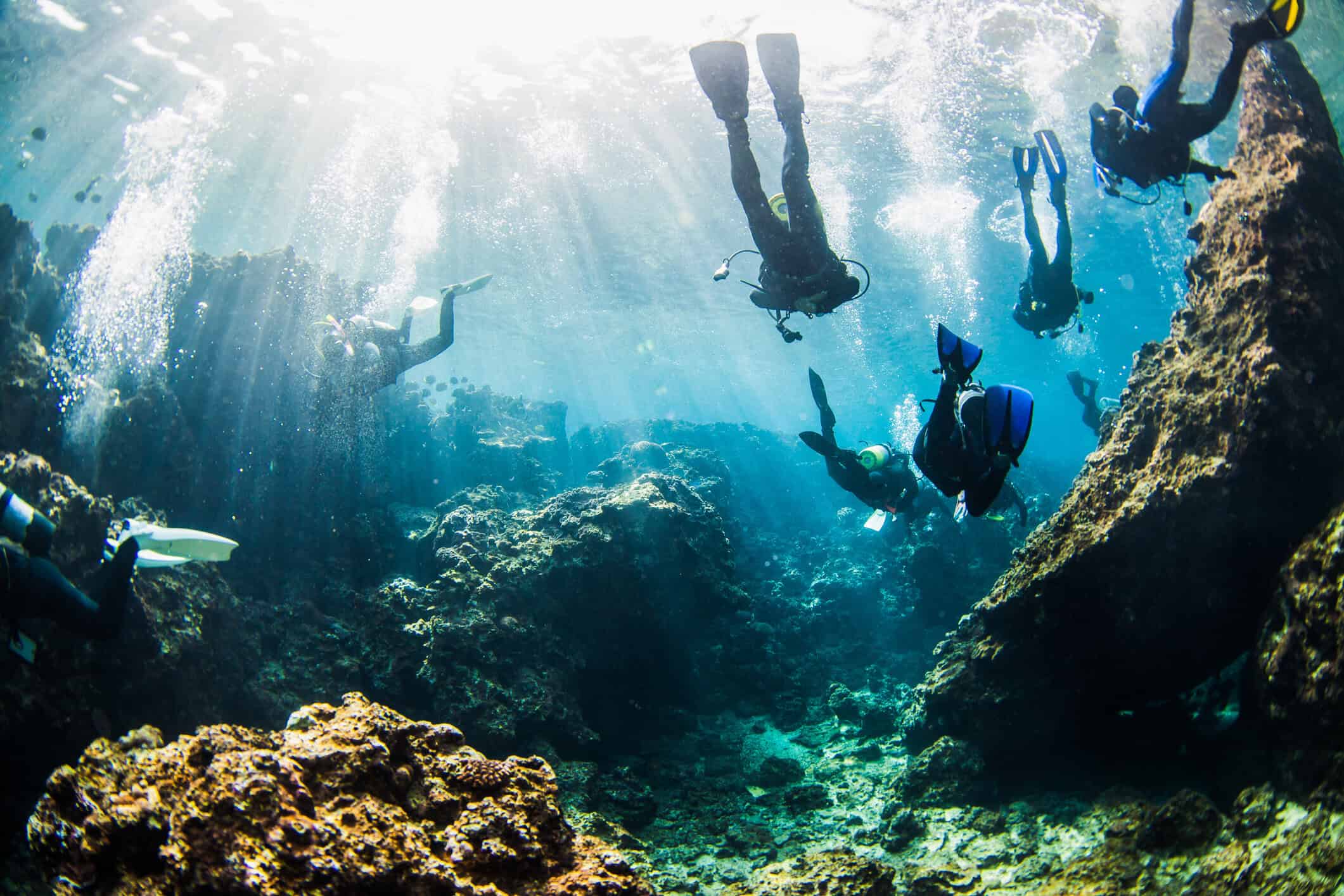 A single scuba diver suspended in deep blue water beneath shafts of light — scuba diving in Japan
