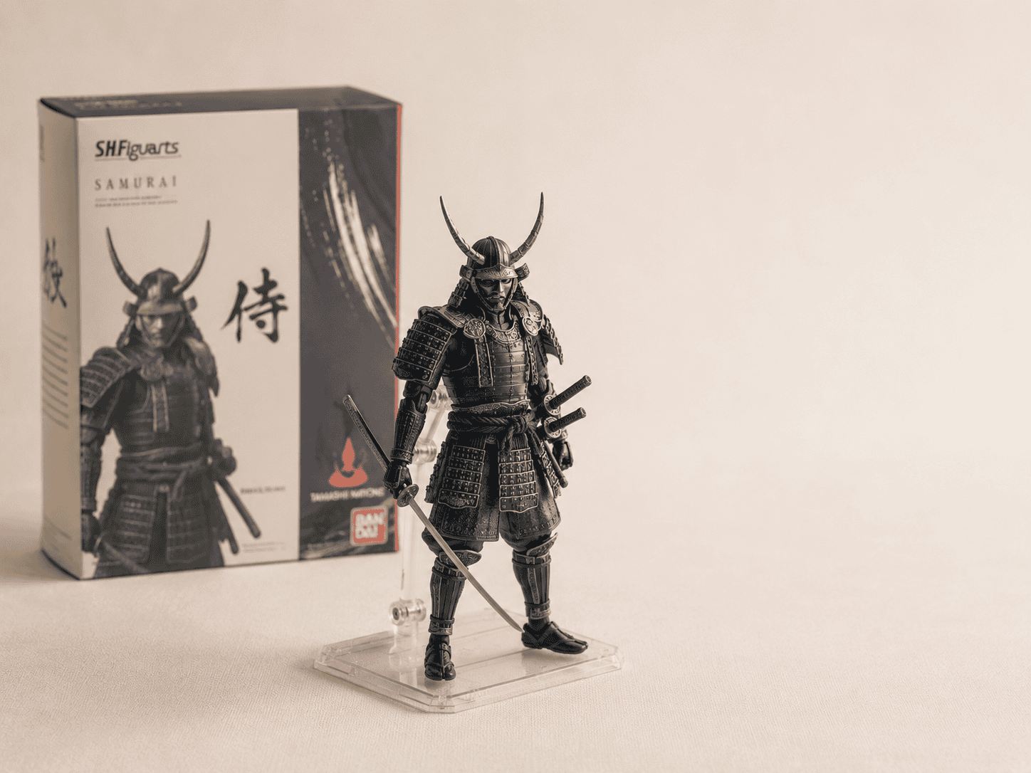 A detailed samurai collectible figure beside its window box on a cream backdrop