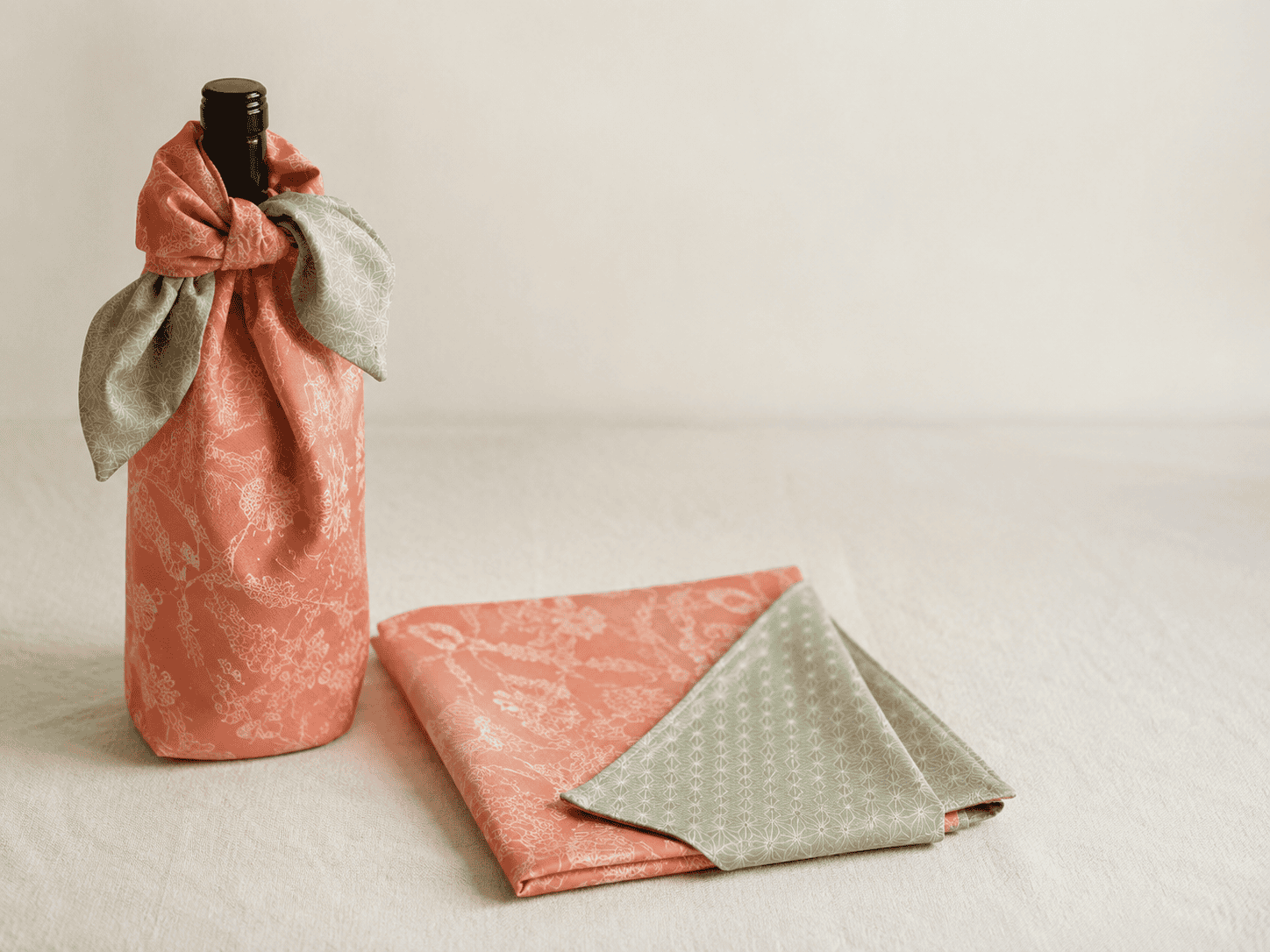 Japanese furoshiki wrapping cloths in apricot and green beside a wrapped bottle