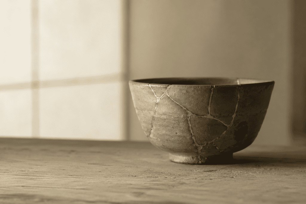 A stoneware tea bowl with gold-mended cracks on a wooden table