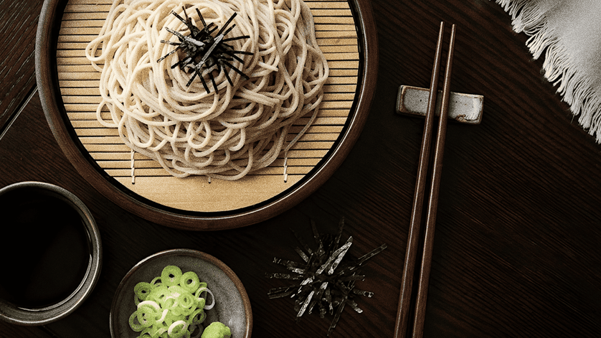 Chilled zaru soba on a bamboo tray topped with shredded nori, with a cup of dipping sauce, spring onion and wasabi