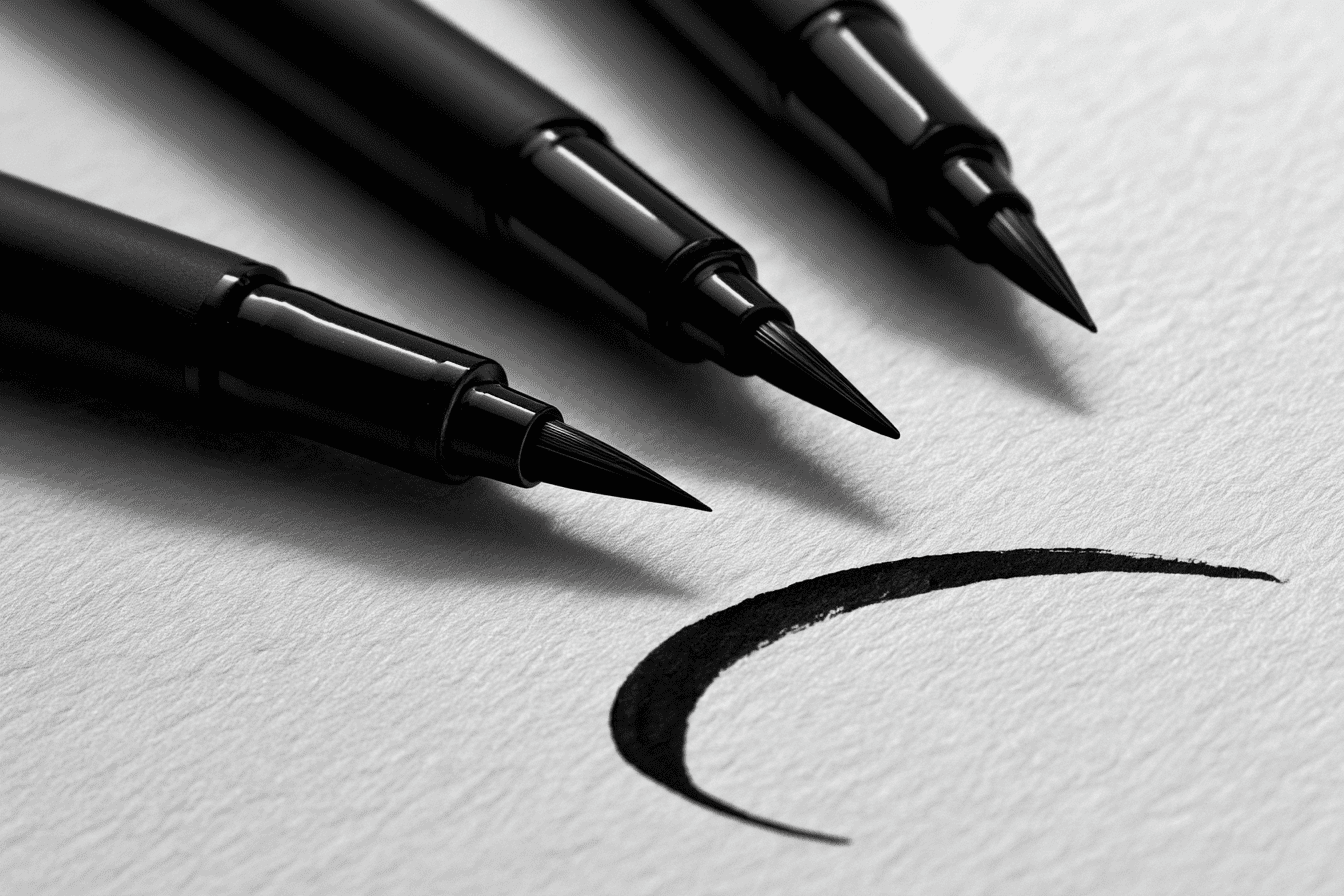 Black brush pens beside a single curved ink stroke on washi paper