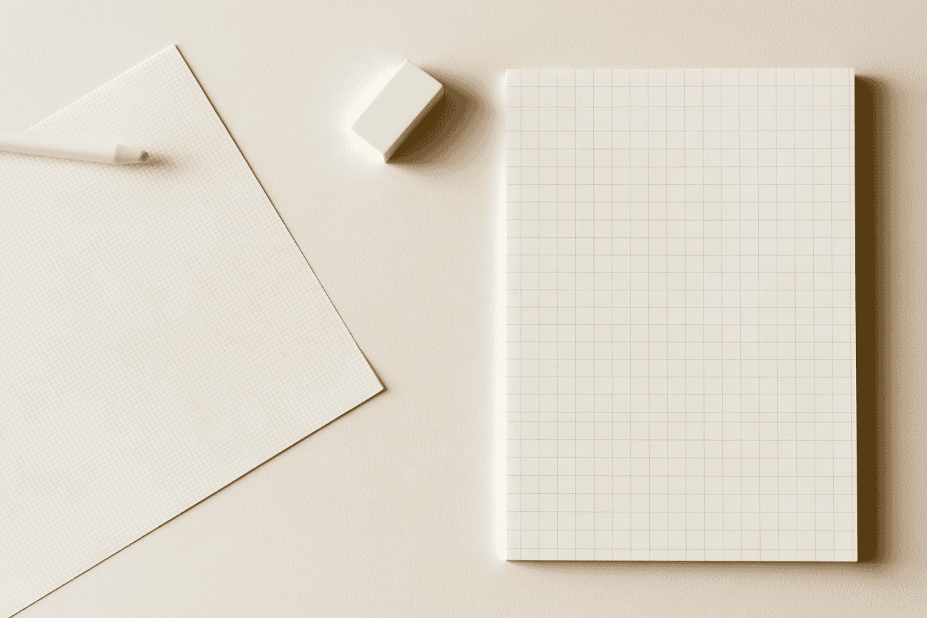 Blank square-grid manuscript paper and a precision eraser on a cream desk