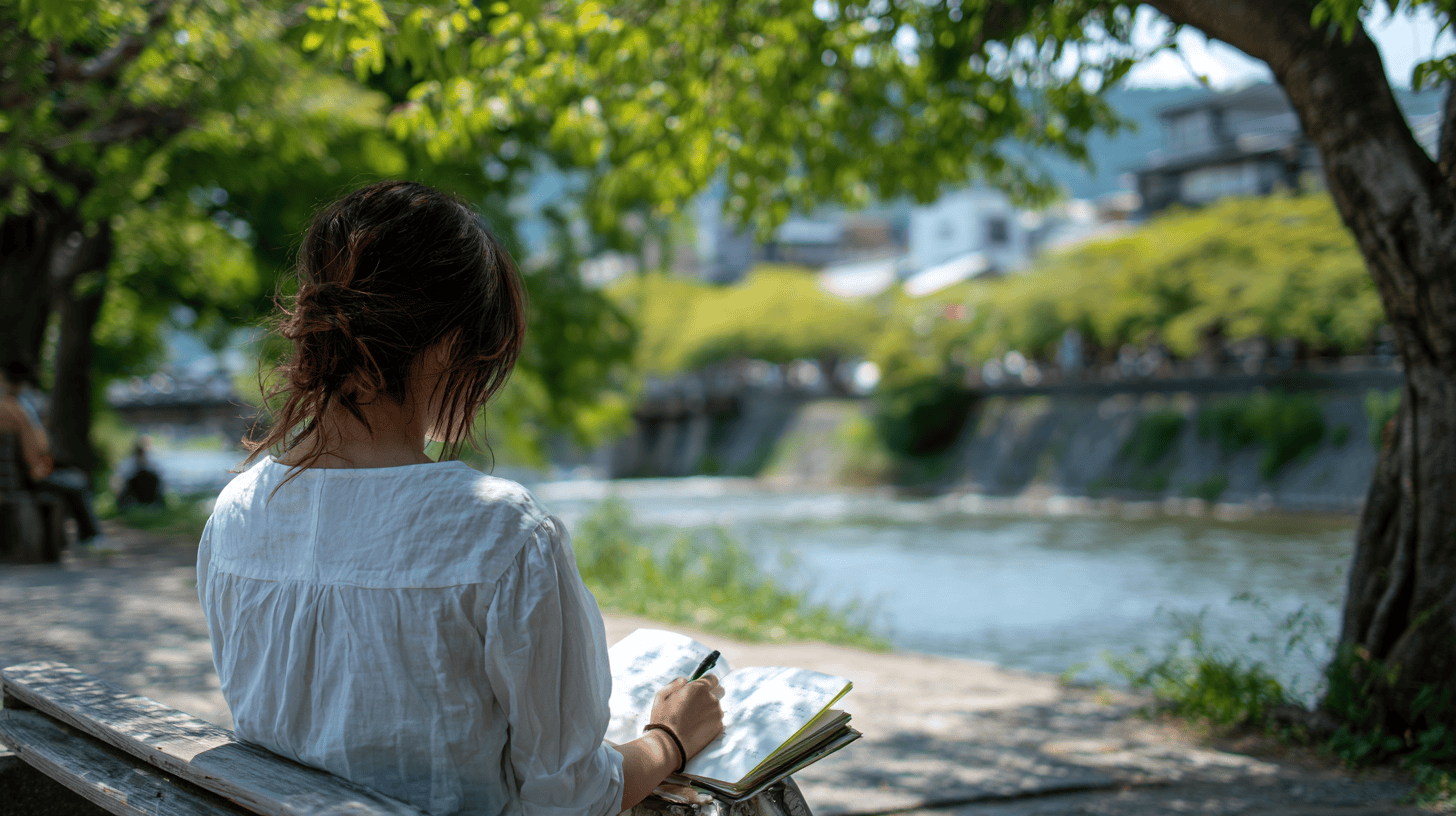 A woman writing in a journal on a sunny riverside bench in Kyoto