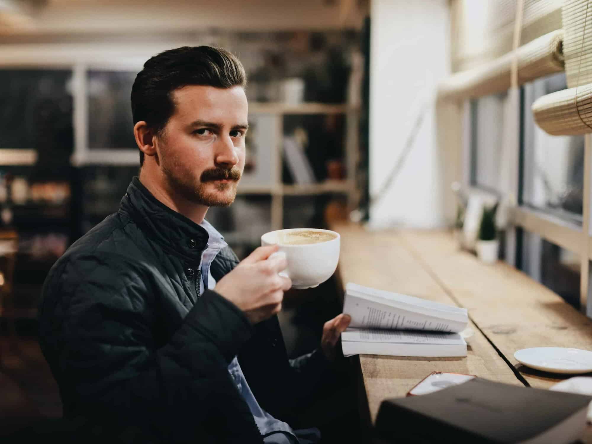A smiling man in a leather jacket holds a white coffee cup at a sunny window table, the kind of dad Japanese gifts for dad are made for