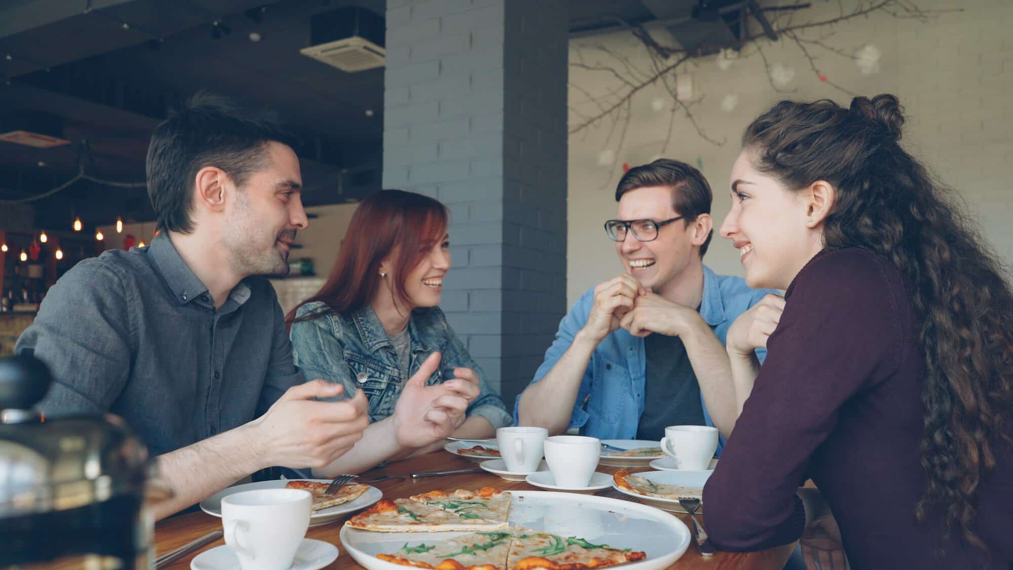 Four friends laughing and talking over coffee and pizza at a cafe table, the kind of evening Japanese gifts for friends lead to