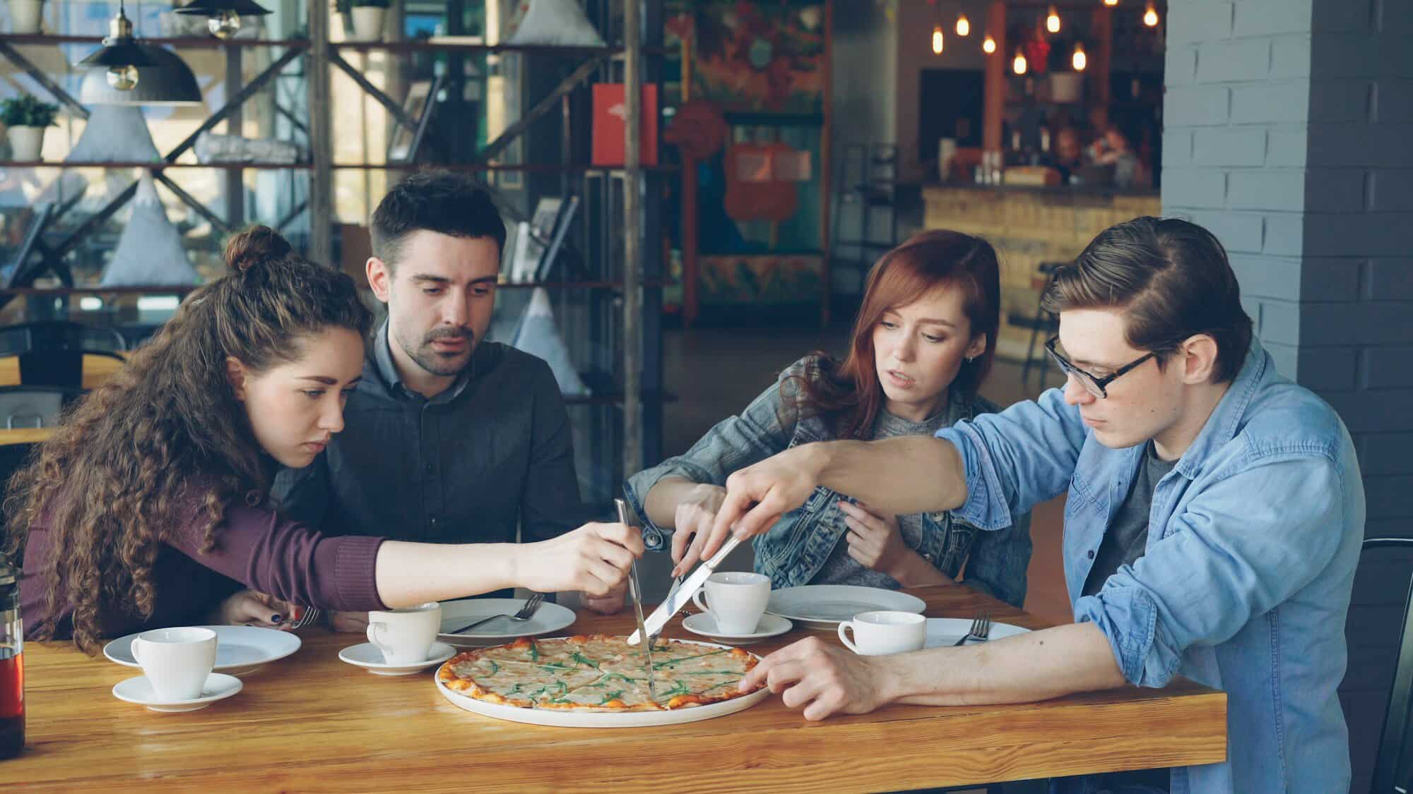 Four friends sharing pizza and conversation around a cafe table