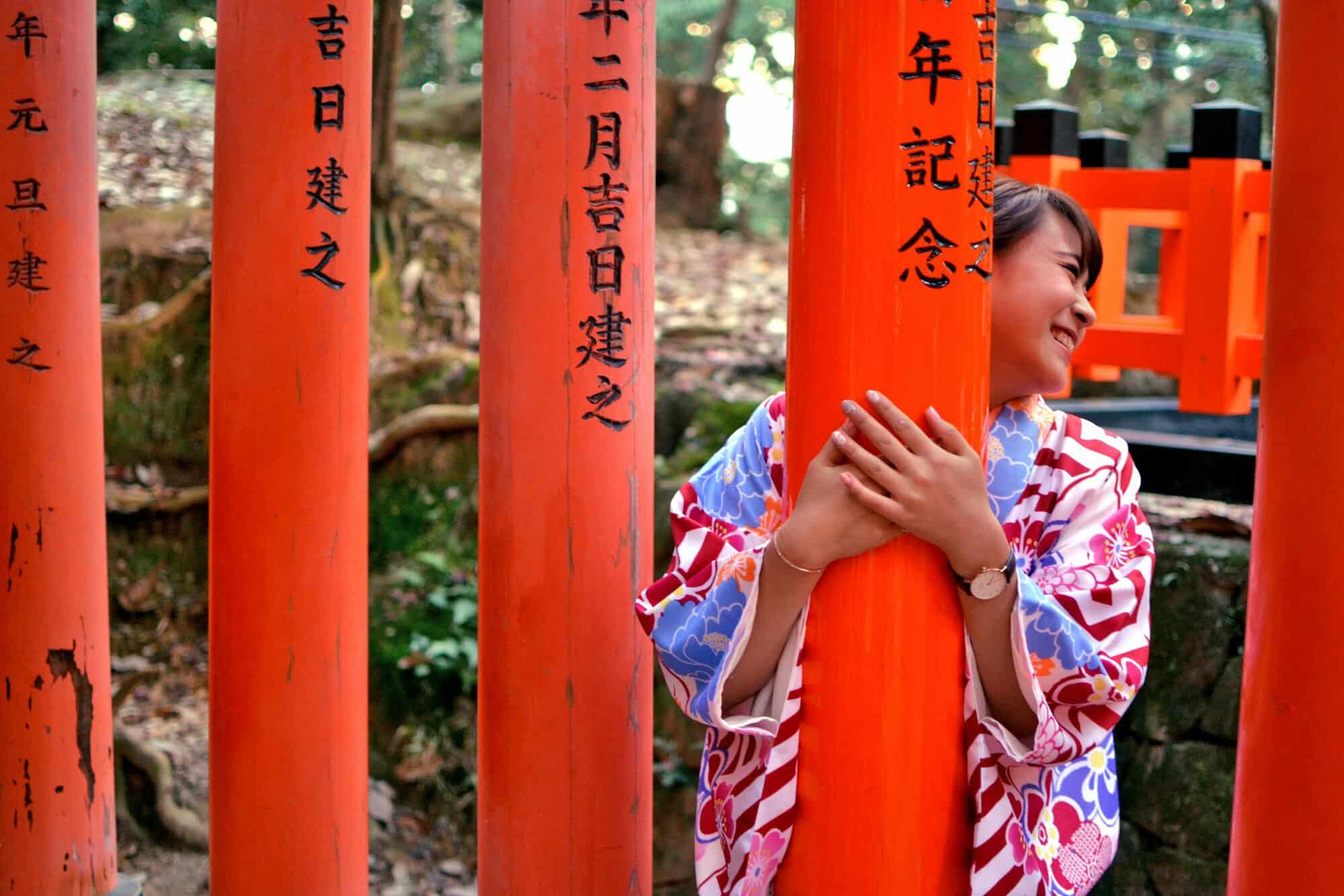A smiling woman in a cotton kimono hugs a bright red gate post in Kyoto, a scene that inspired these Japanese gifts for her