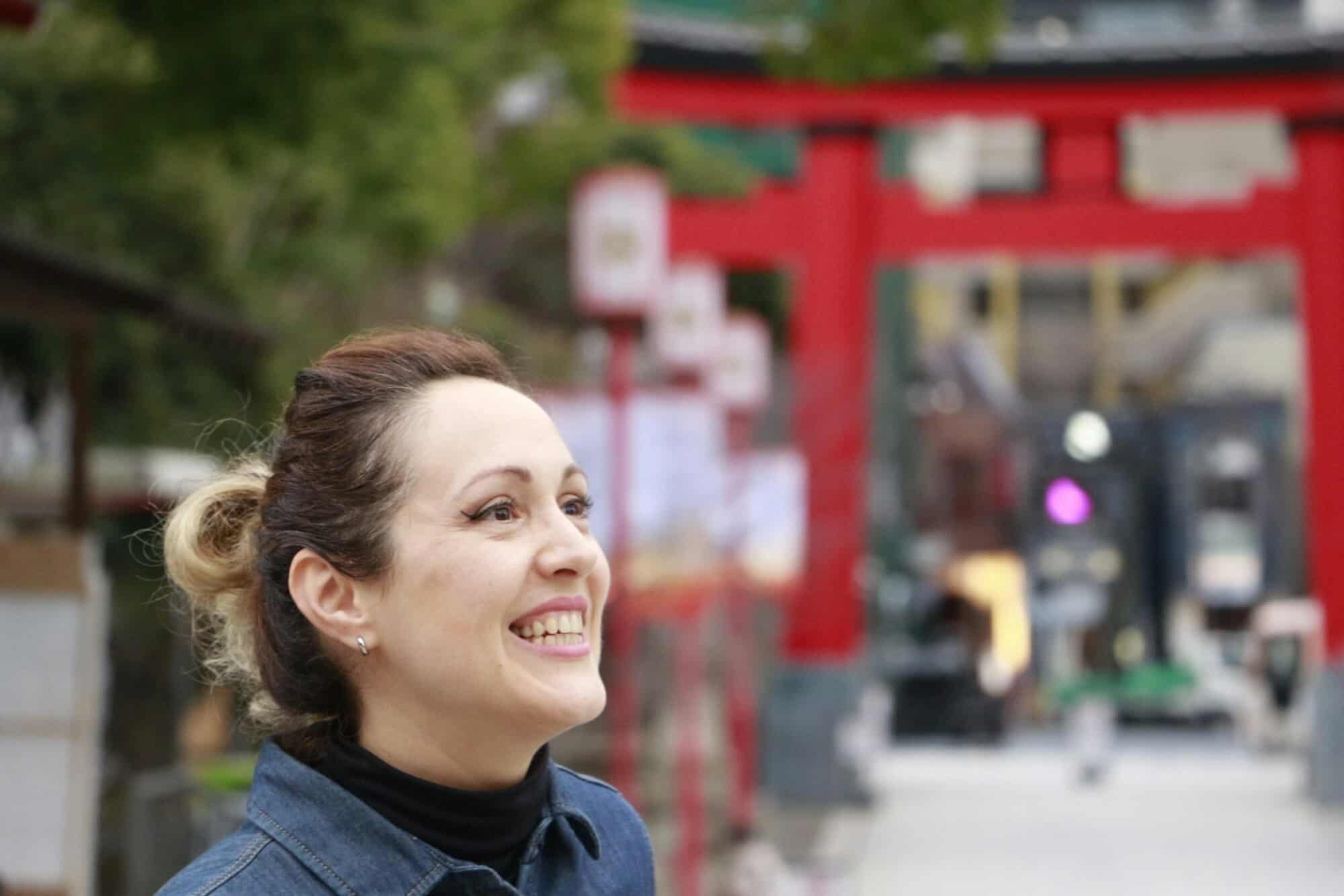 A smiling woman in a dark sweater in front of a red gate and lanterns, the kind of person gifts for the Japan lover are chosen for