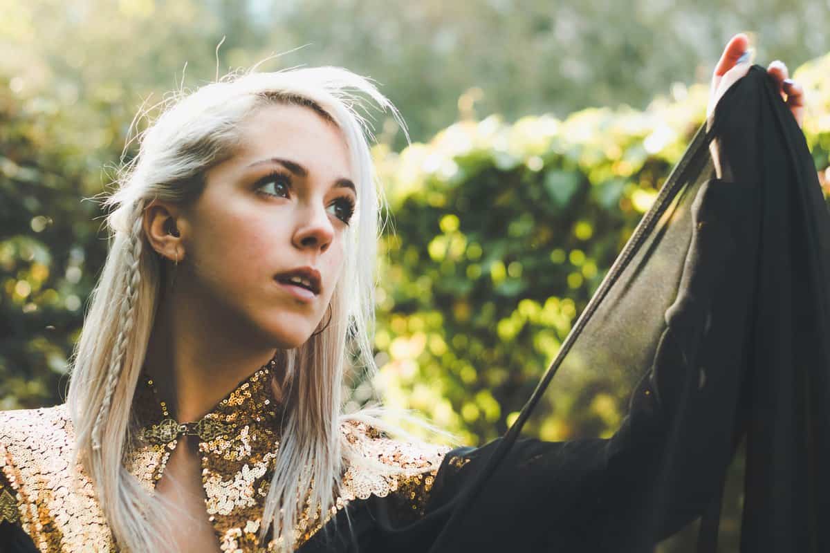 A blonde woman holding up a length of dark fabric in a sunlit garden