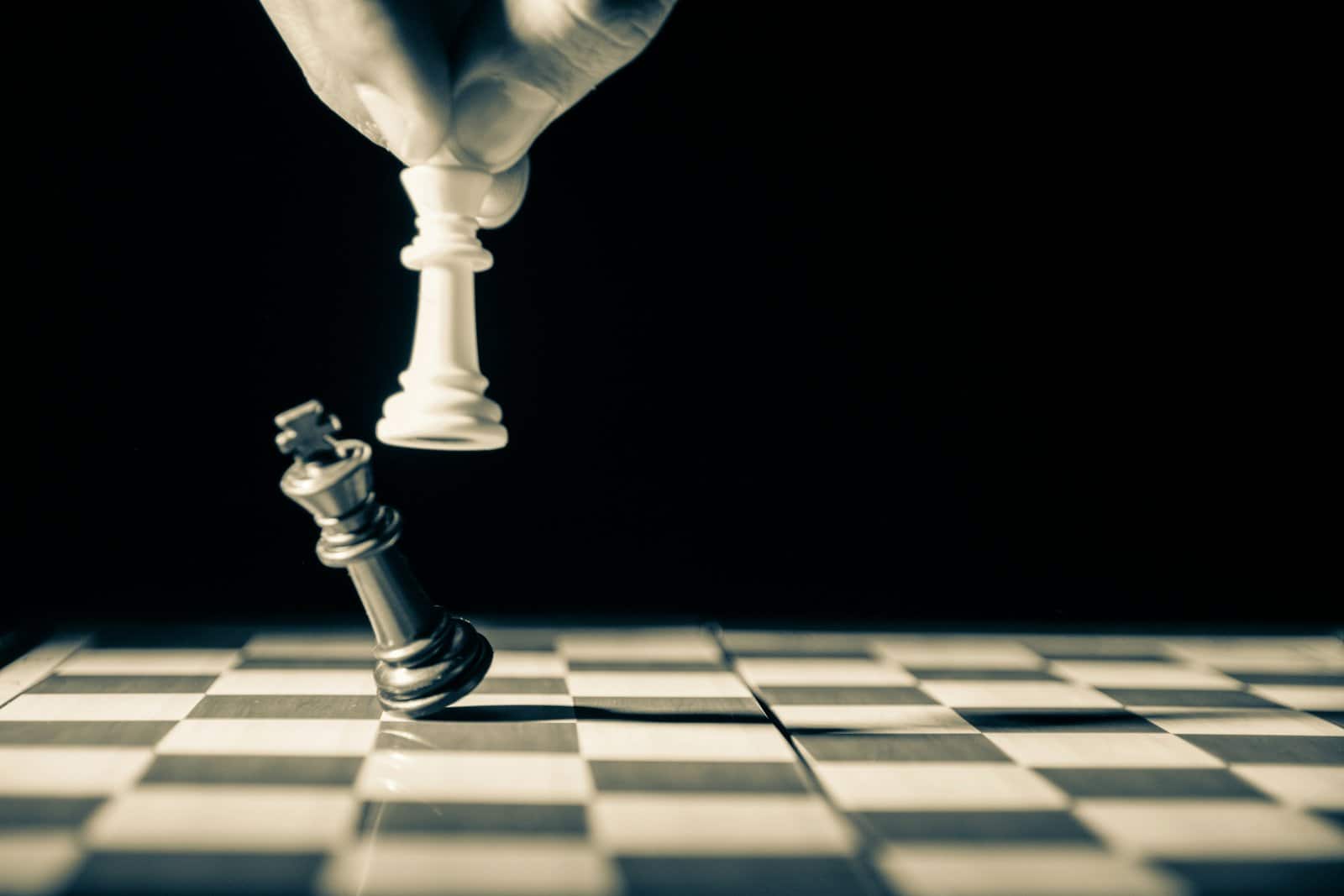 A hand lifting a white chess king above a toppled black king on a checkered board, a reset of the position after a loss