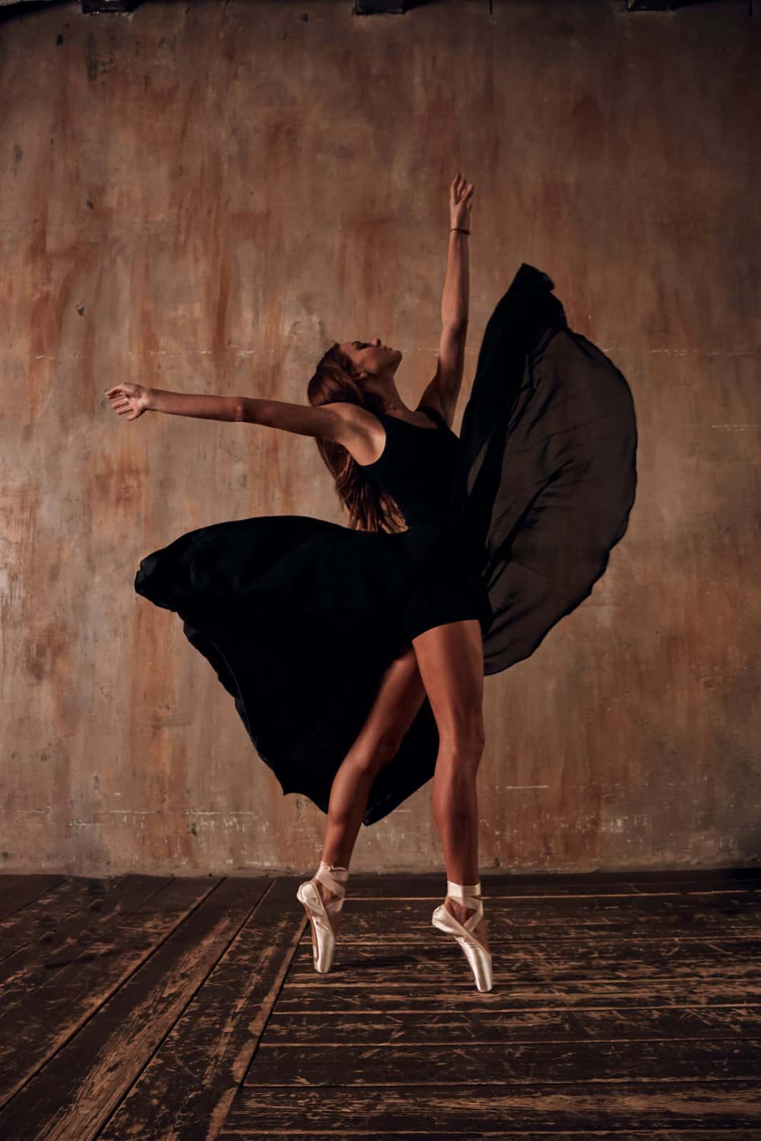 A ballet dancer in a black dress and pointe shoes leaning back in an open pose in a warm studio, a picture of returning to yourself