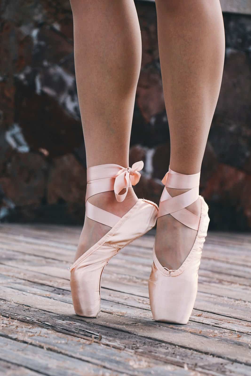Close view of a dancer’s feet in pale pink pointe shoes tied with ribbon on a wooden floor, the discipline of small repetition
