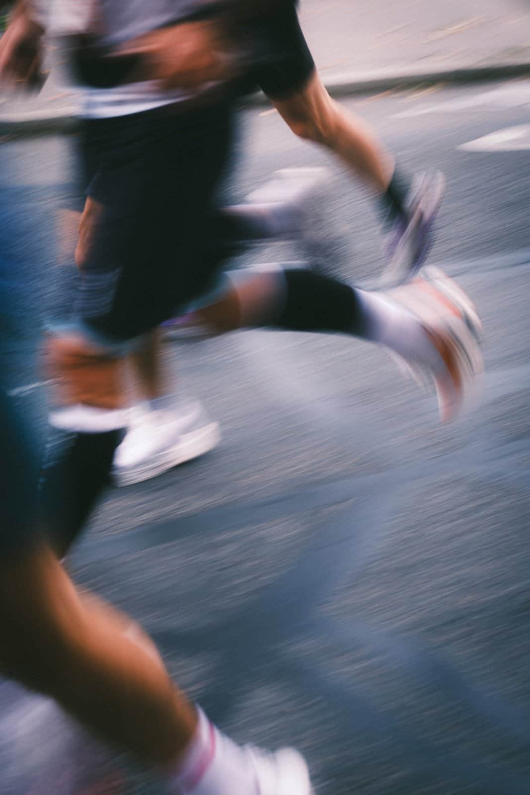 Motion-blurred runners’ legs and shoes on a city road, momentum built one step at a time