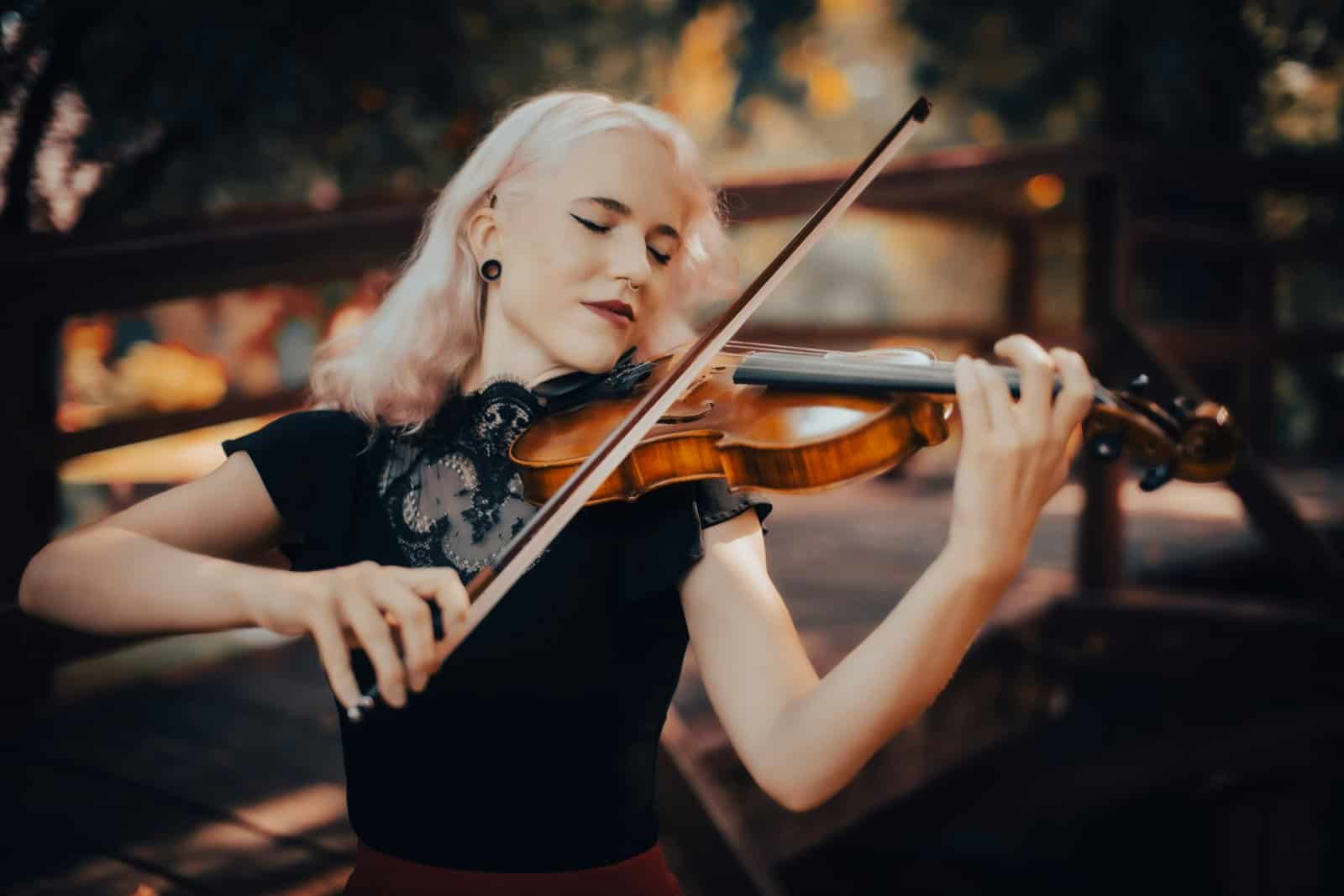 A violinist with pastel hair and closed eyes playing on a wooden bridge among autumn trees, harmony found in the doing