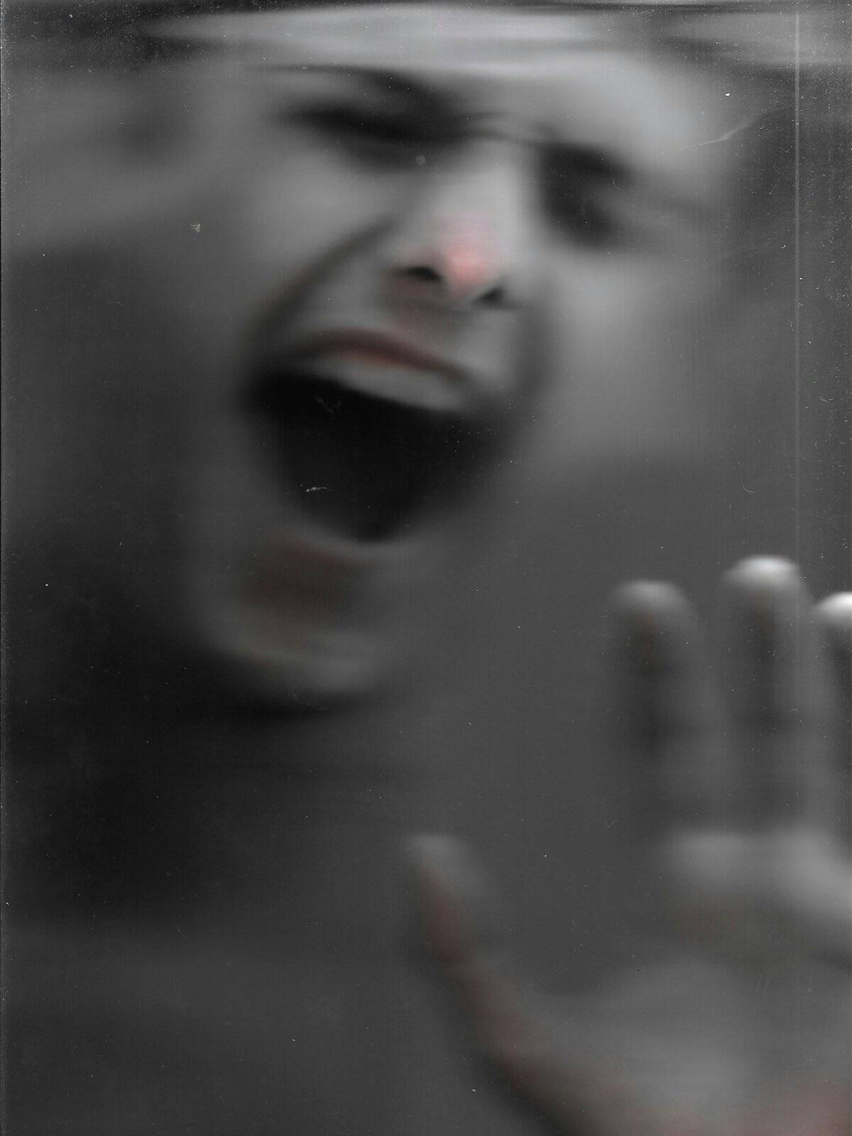 A blurred black-and-white figure pressing a hand against glass with an open mouth, the distance felt when missing them