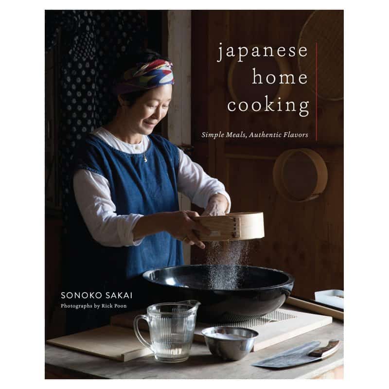 The cover of Japanese Home Cooking by Sonoko Sakai showing the author sifting flour in a kitchen