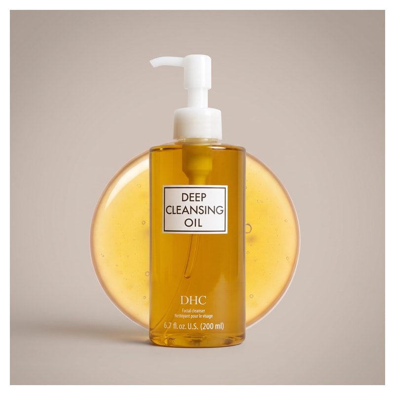 A clear bottle of DHC Deep Cleansing Oil with a pump top on a warm background