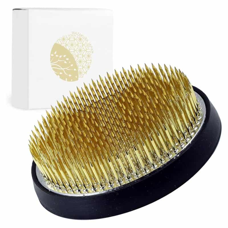 A round brass ikebana kenzan with closely set steel pins on a white background