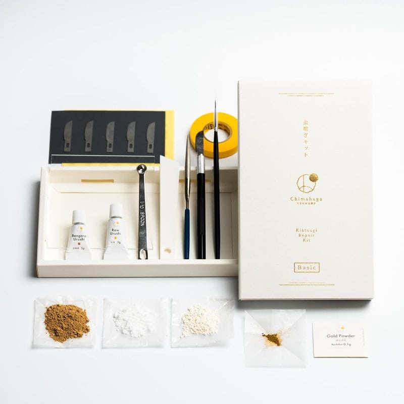 A Chimahaga kintsugi repair kit with lacquer tubes, brushes and gold powder laid out on white