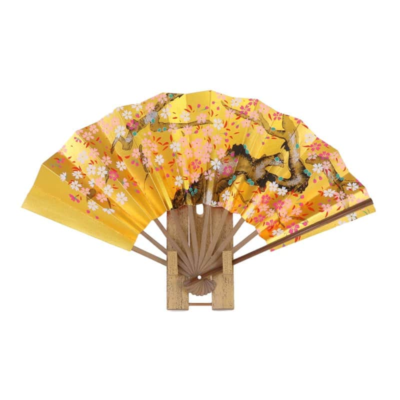A Kyoto folding fan painted with pink cherry blossoms on gold paper, standing on its display stand