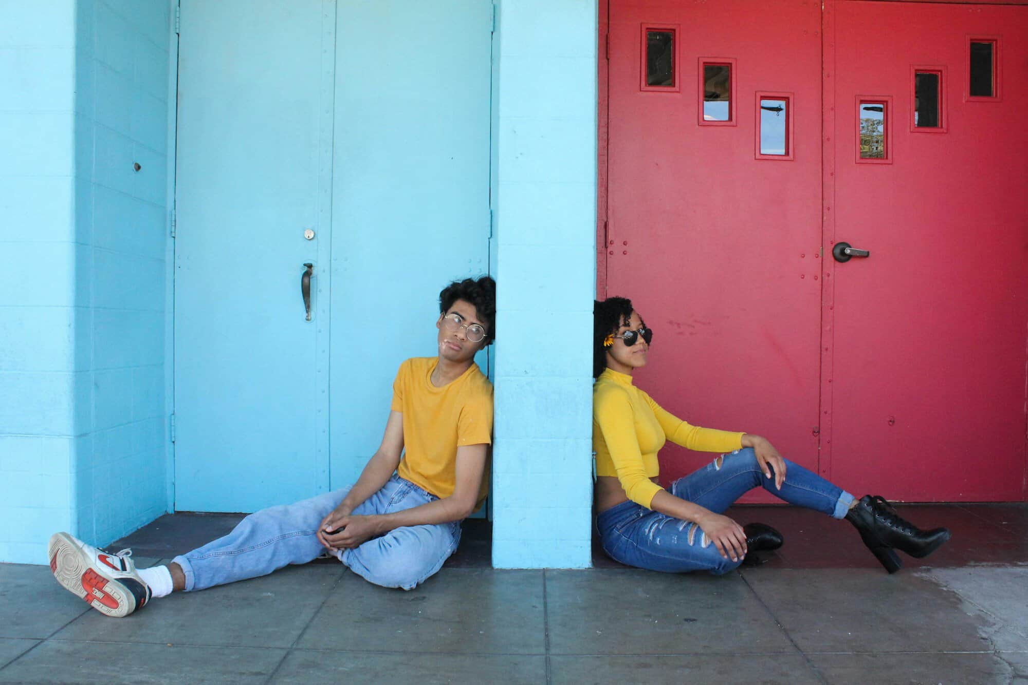 Two smiling teenagers sitting against a bright turquoise and red wall in yellow tops, the kind of friends Japanese gifts for teens are made for